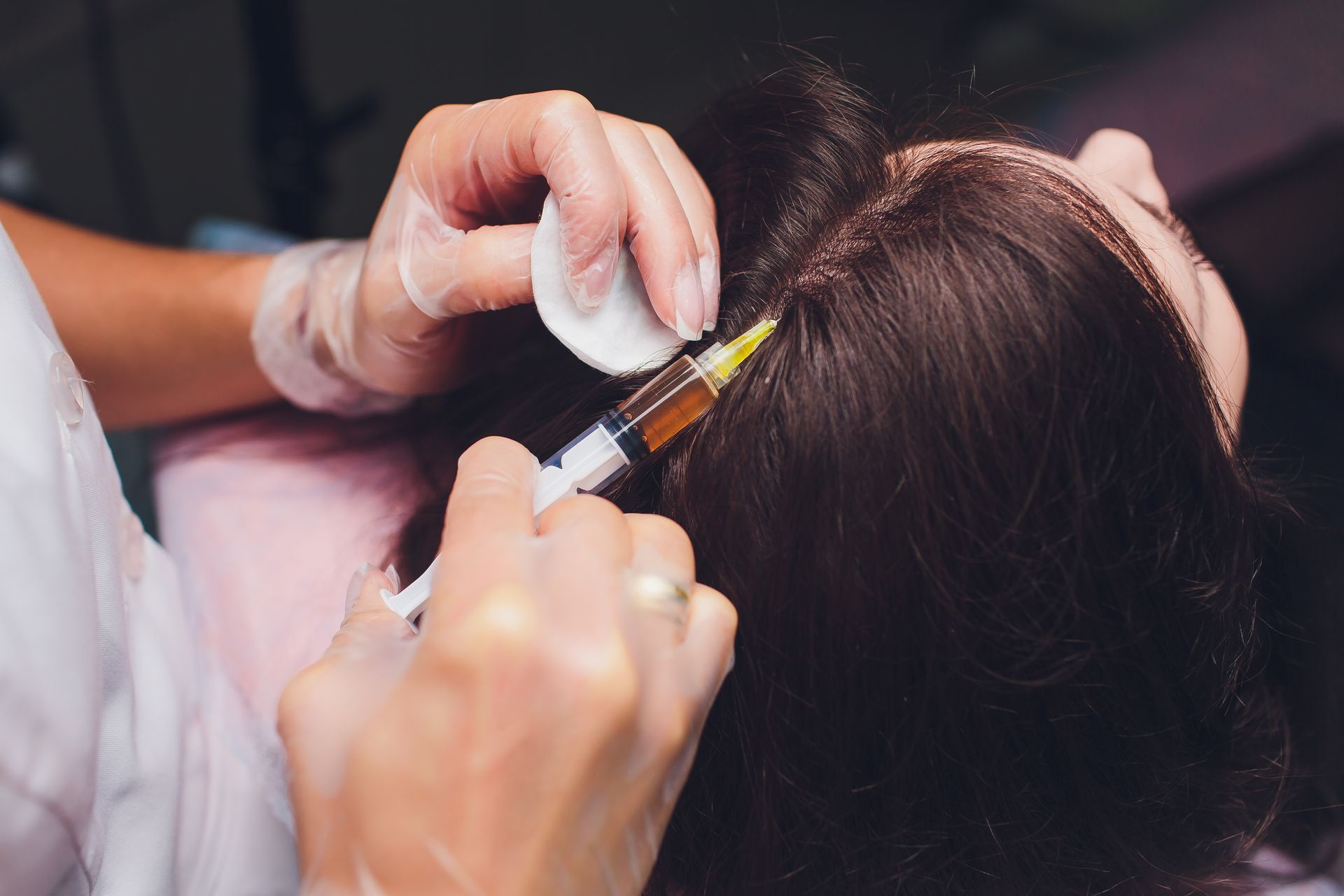 Hands parting dark hair while applying dye with a brush and mixing bowl in a salon