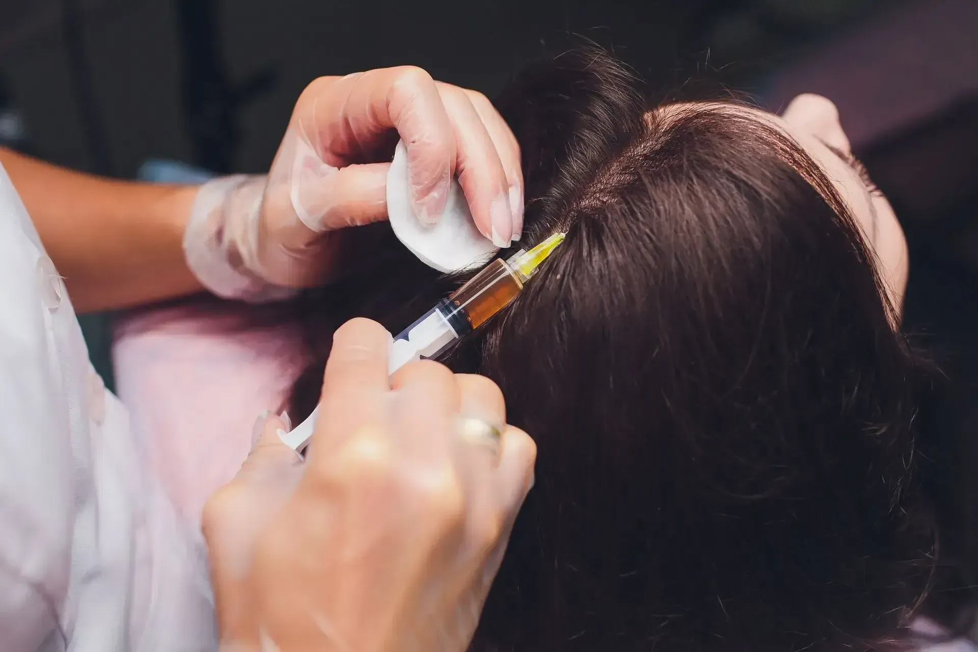 Hands parting dark hair while applying dye with a brush and mixing bowl in a salon