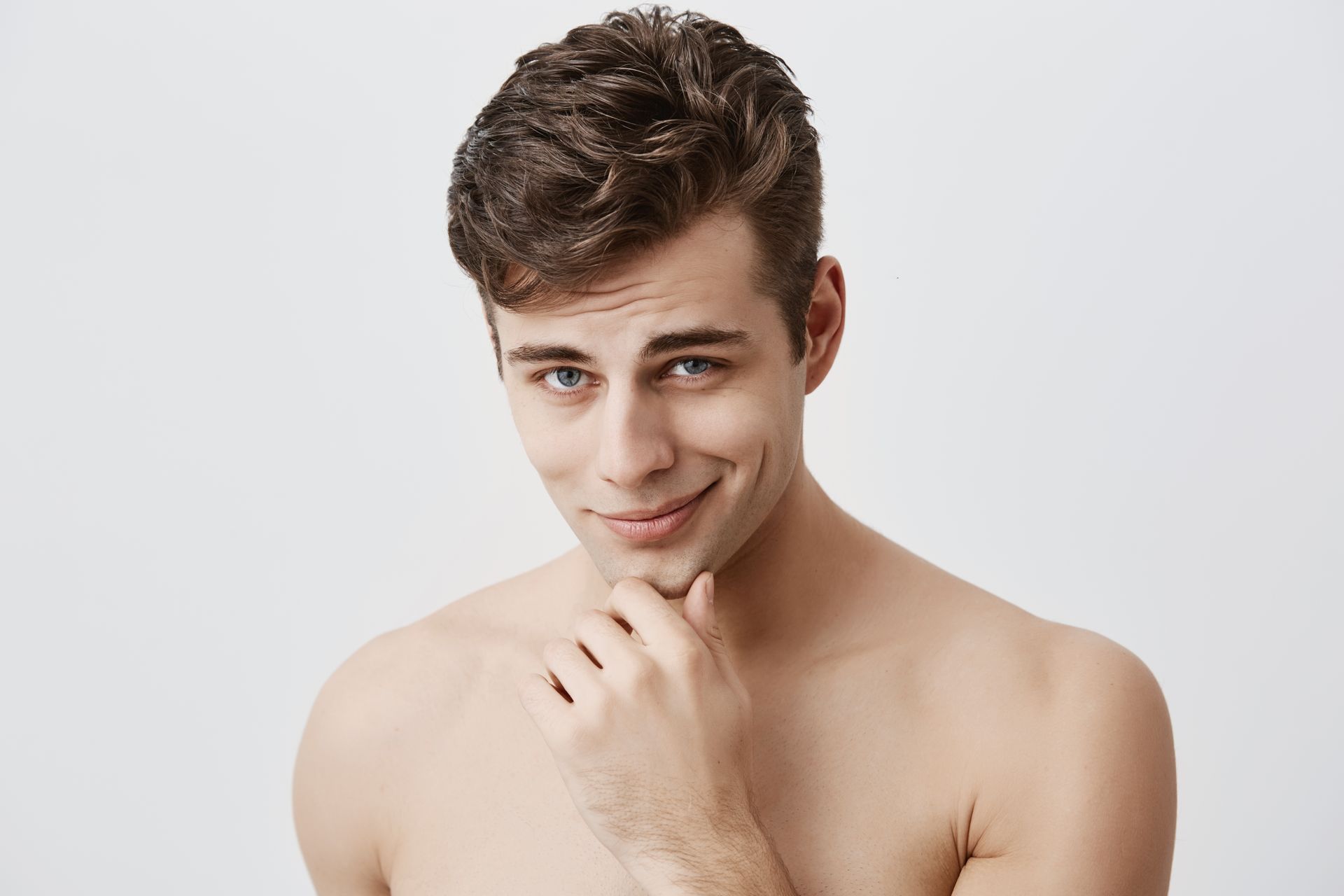 A shirtless young man is smiling with his hand on his chin.