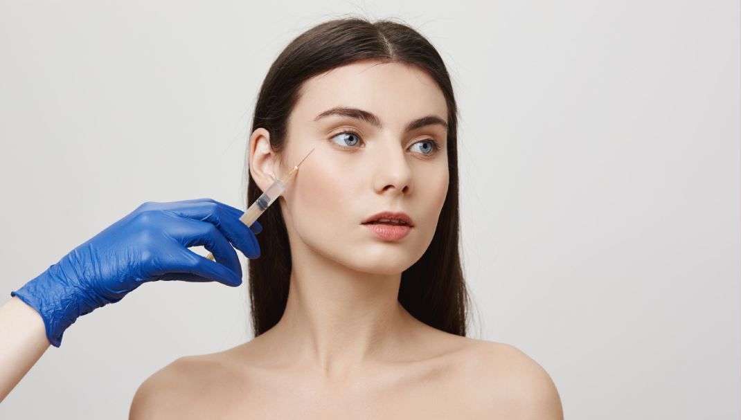 Close-up of a hand injecting dermal fillers into a woman's eye area.
