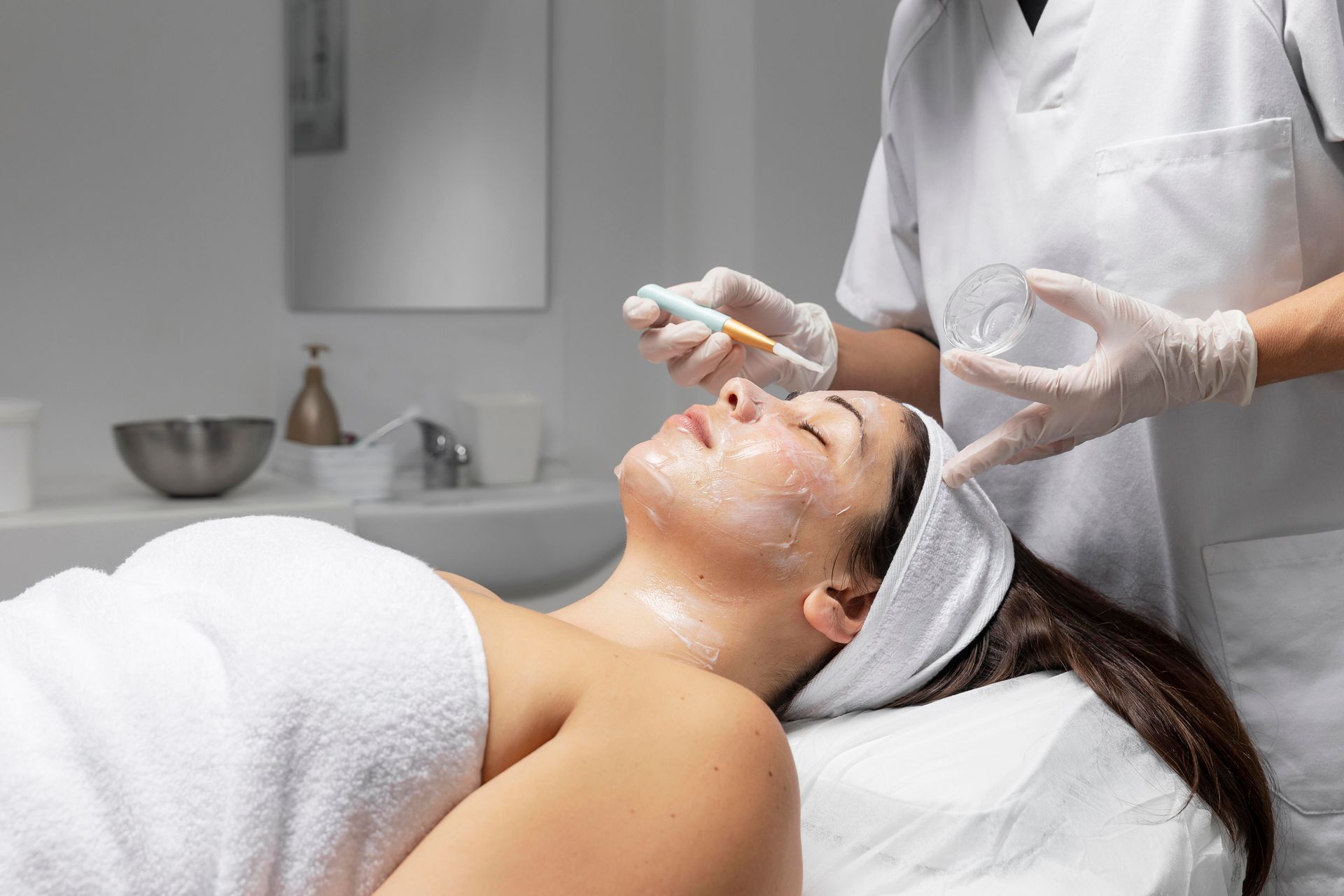 Esthetician applying facial treatment to a reclining client in a spa treatment room