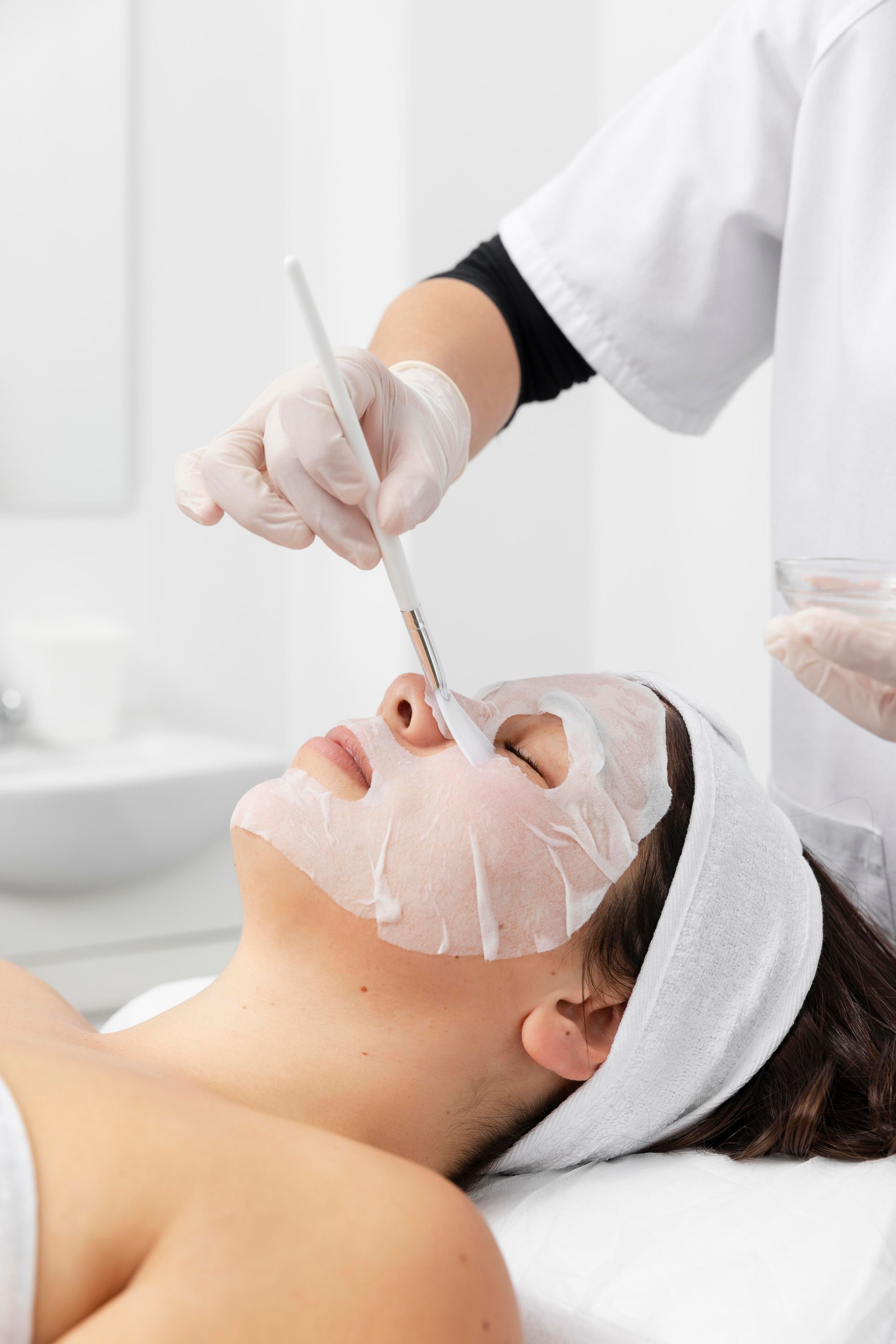 Facial treatment with a cream mask applied by a gloved esthetician in a spa setting