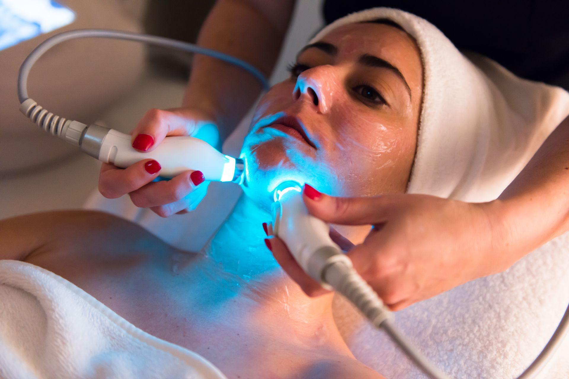 Woman receiving a glowing blue facial treatment with handheld devices in a spa setting