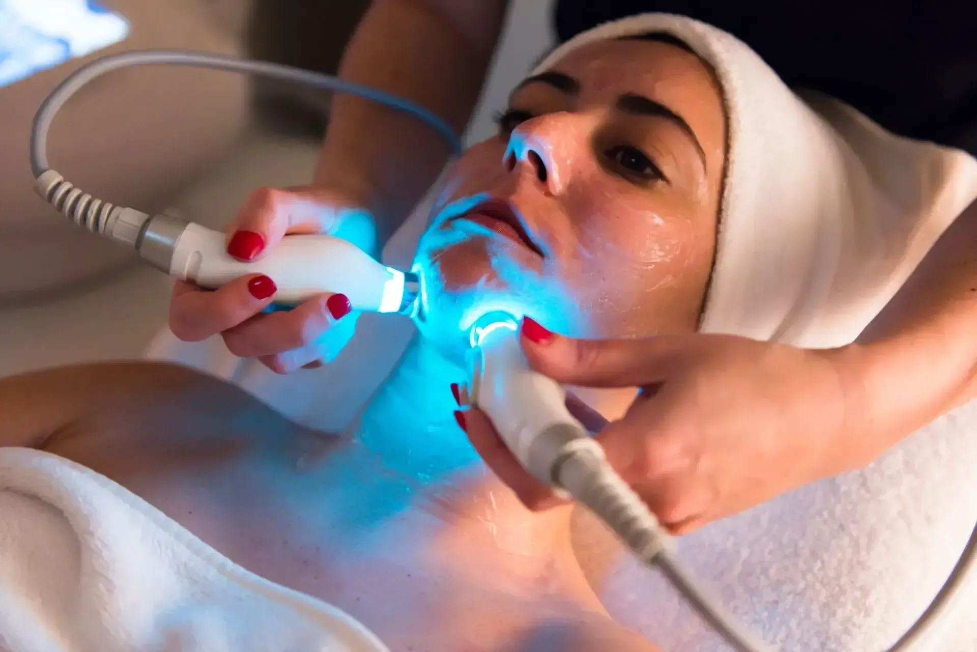 Woman receiving a glowing blue facial treatment with handheld devices in a spa setting