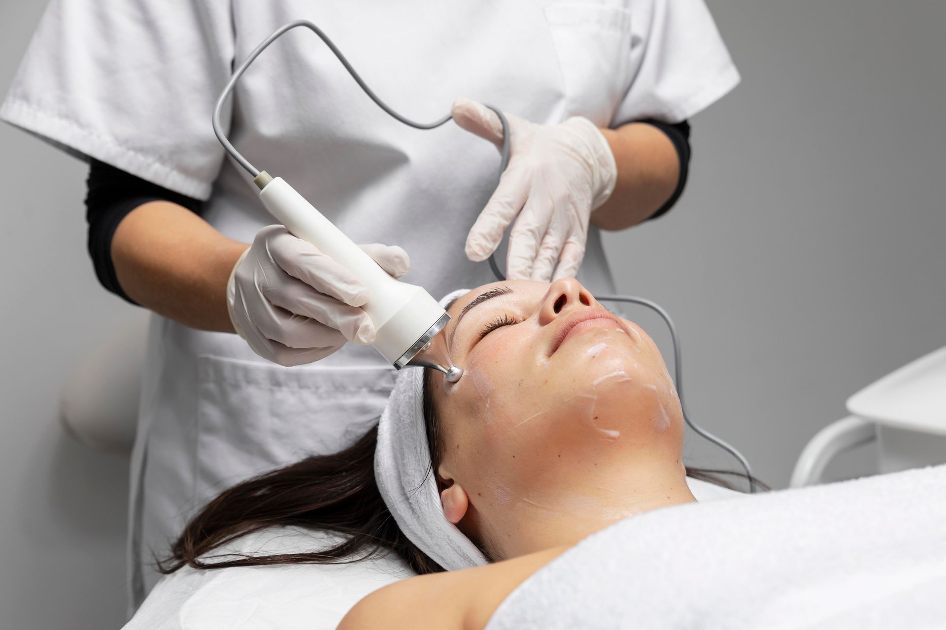 Cosmetic facial treatment with a handheld device on a reclining client wearing a headband and gloves