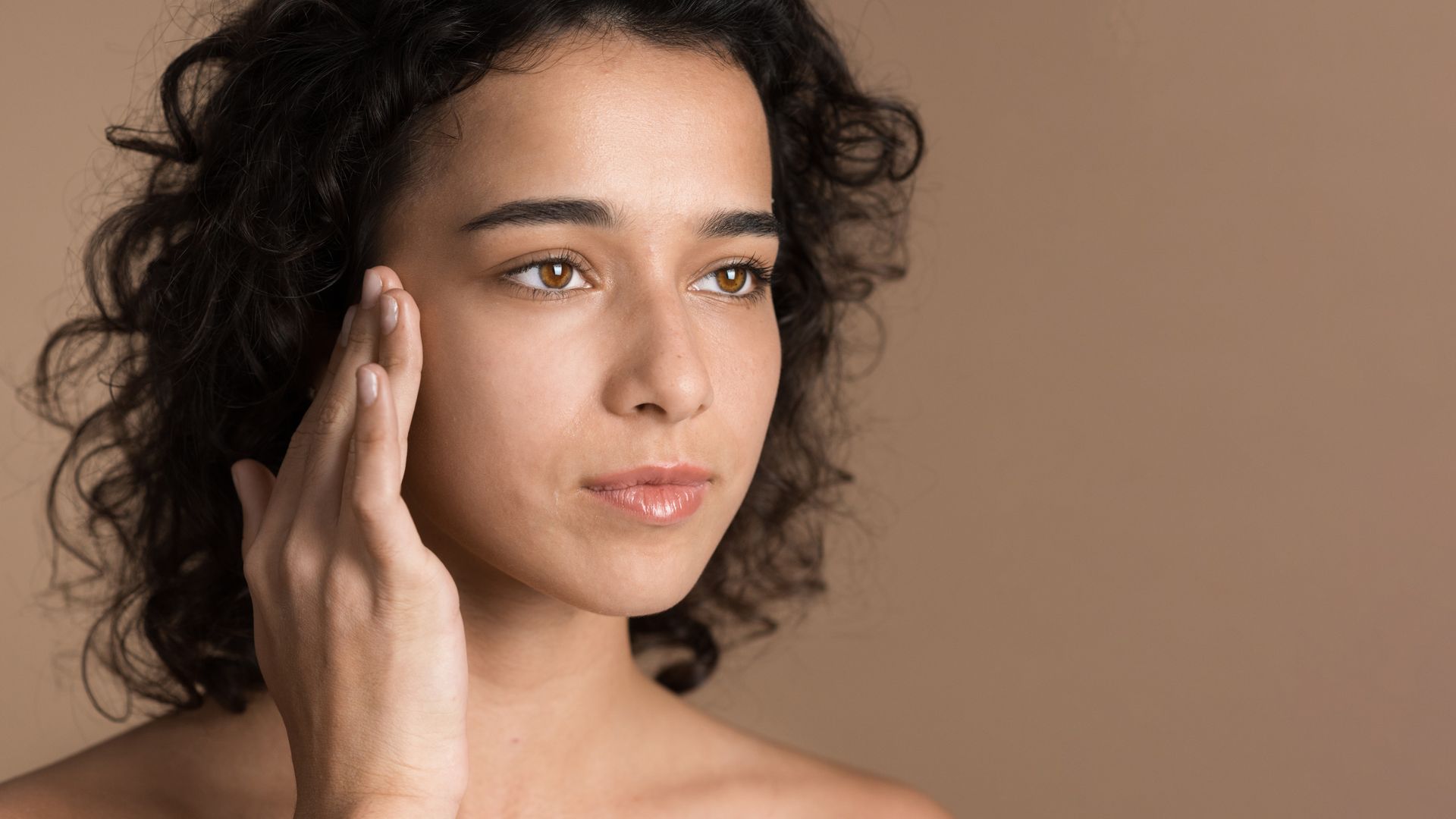a woman with curly hair touches her face with her hand