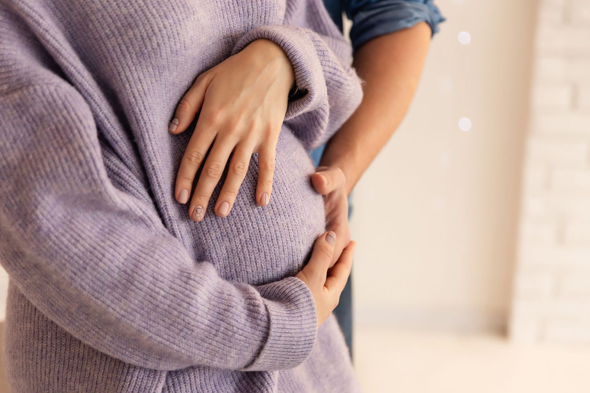 Pregnant person's belly, hands resting on it. Another person's arm on the side.