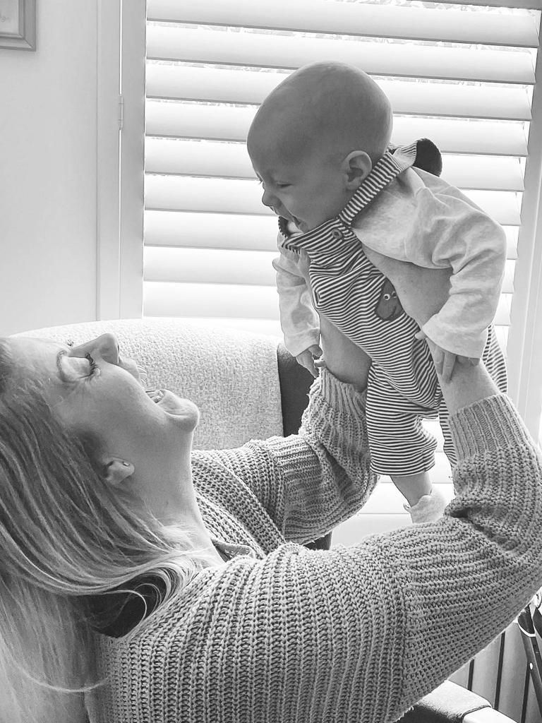 Woman smiling and holding a baby up in the air near a window, black and white photo.