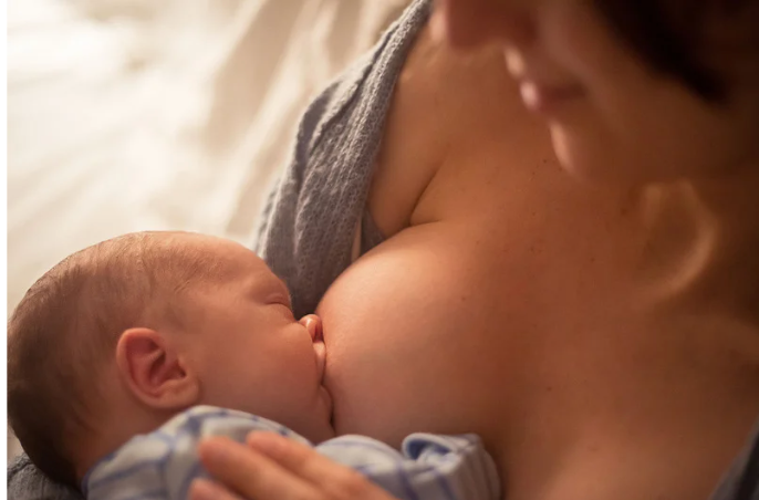 Baby nursing at a person's breast indoors.