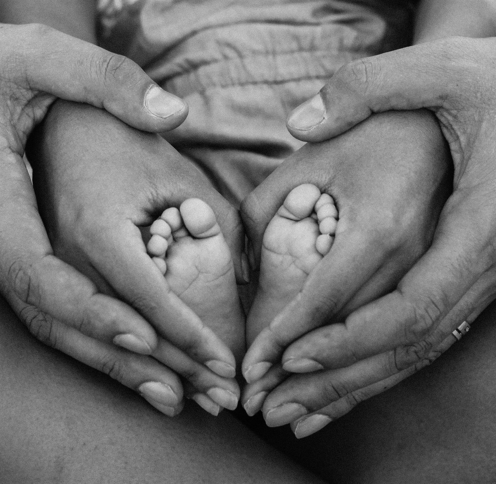Hands cradling baby feet, forming a heart shape.