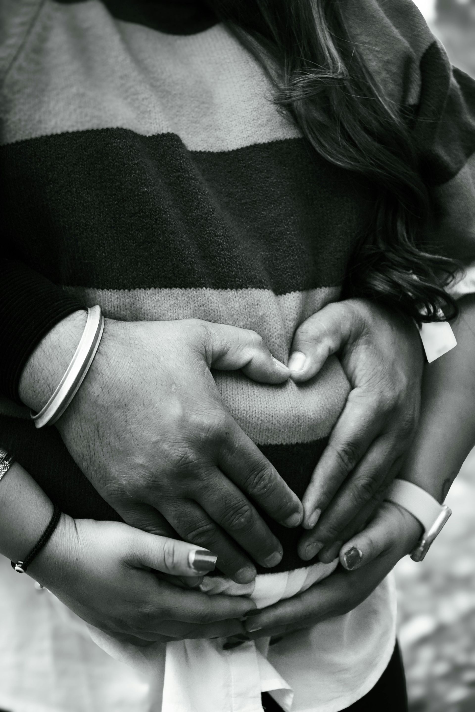 Hands forming a heart shape over a pregnant belly; black and white.