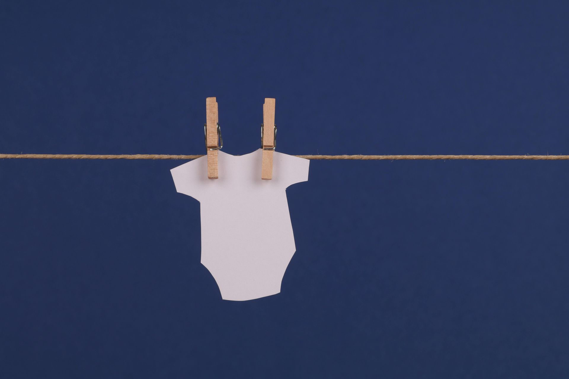 White onesie hanging on a clothesline with wooden clothespins, blue background.