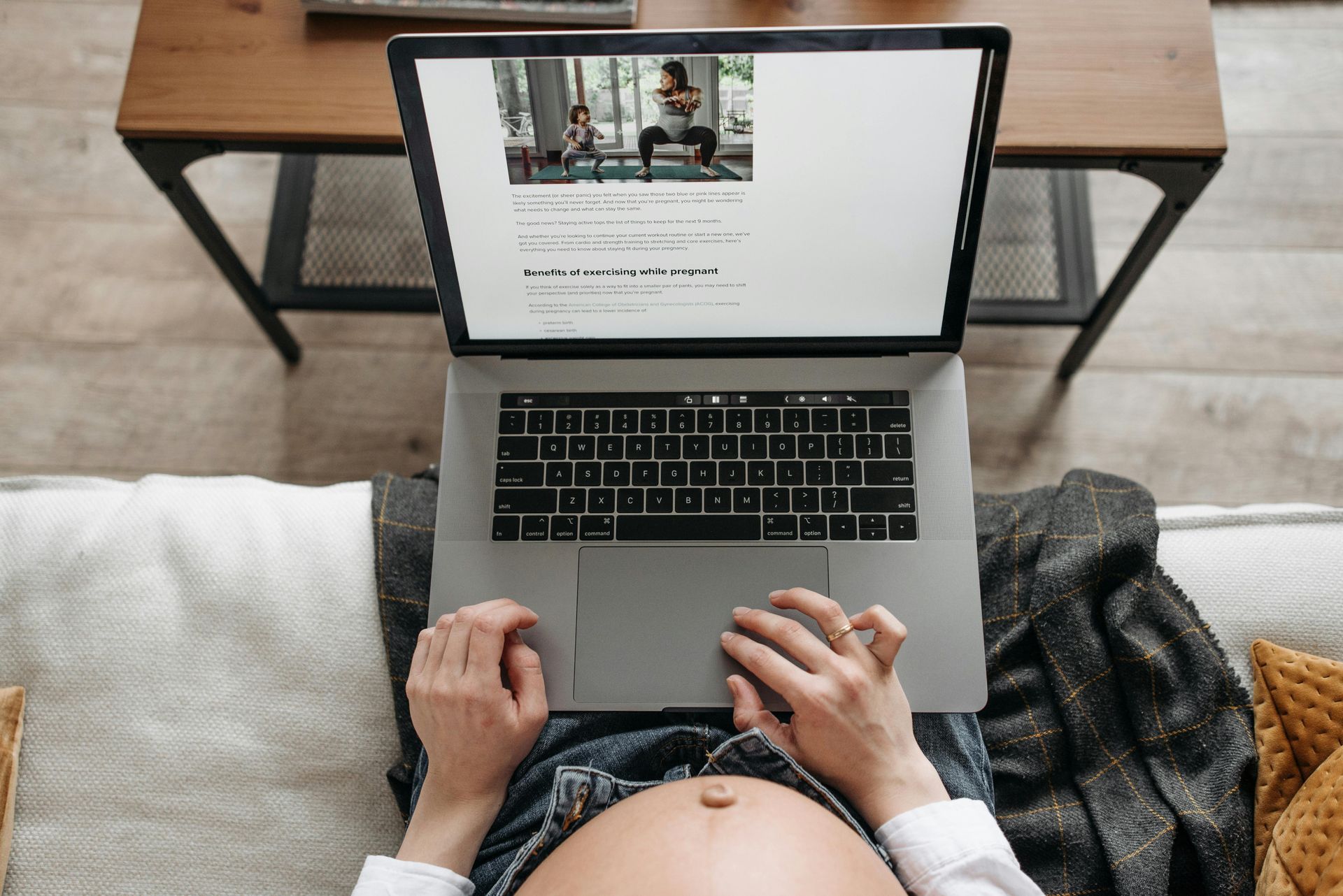Pregnant person using a laptop, possibly viewing workout instructions; indoors on a couch.