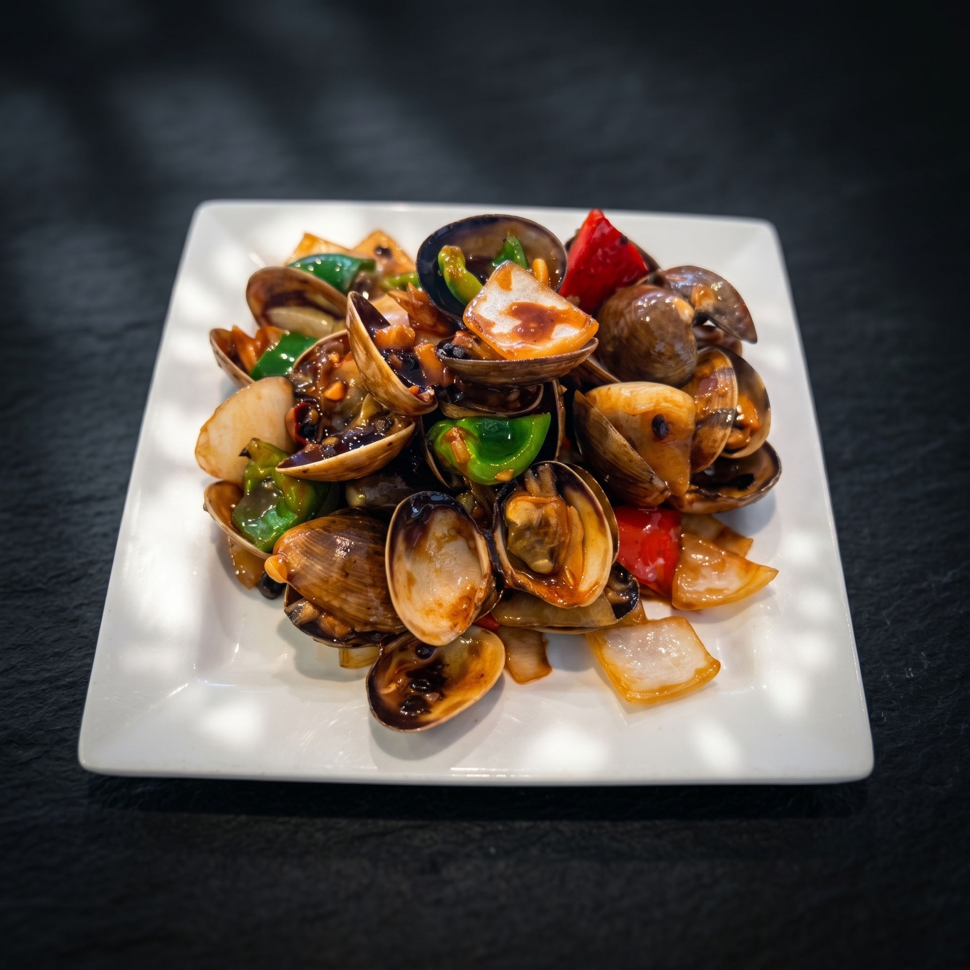 Stir-fried clams with bell peppers and onions on a white square plate