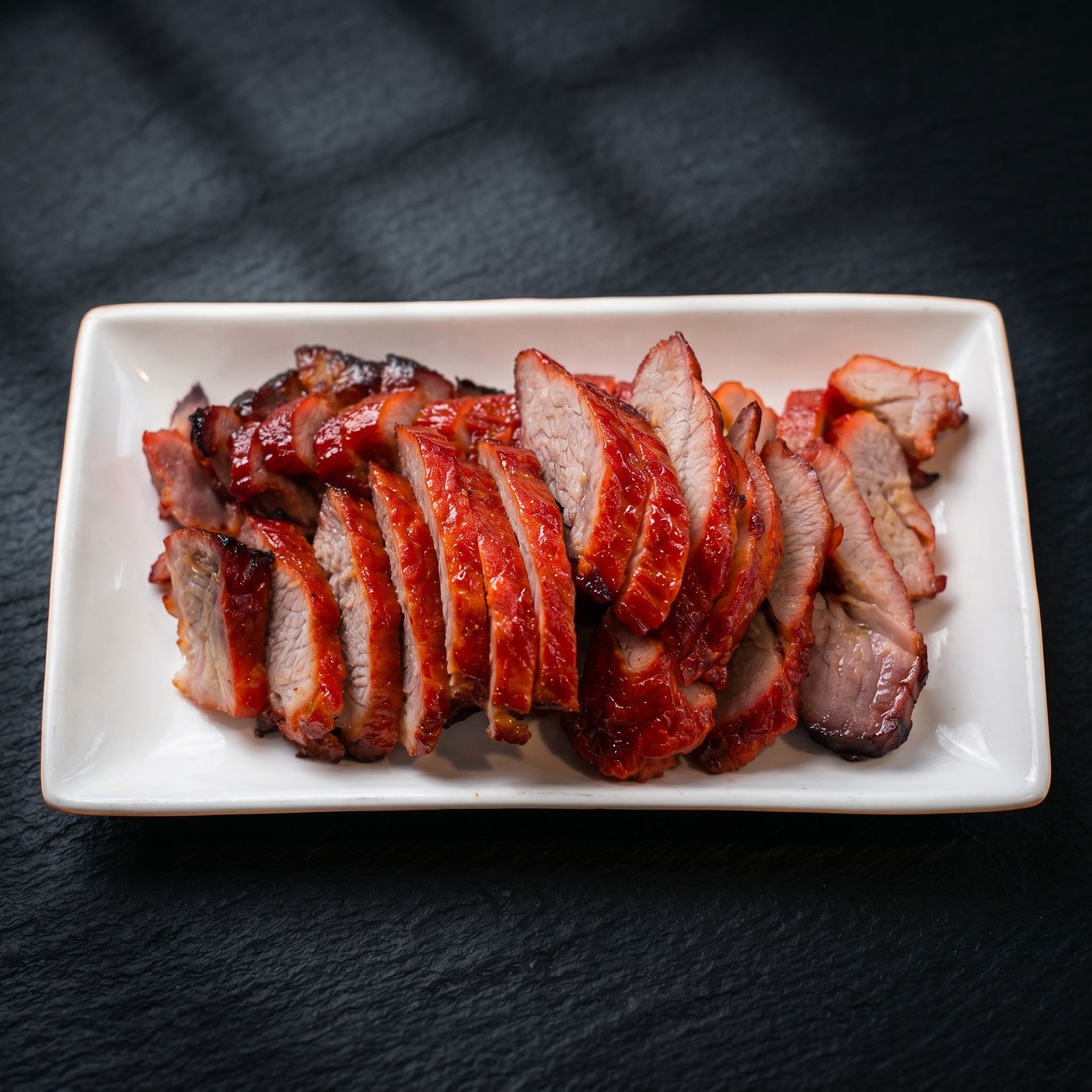 Sliced glazed roasted meat on a white rectangular plate against a dark background