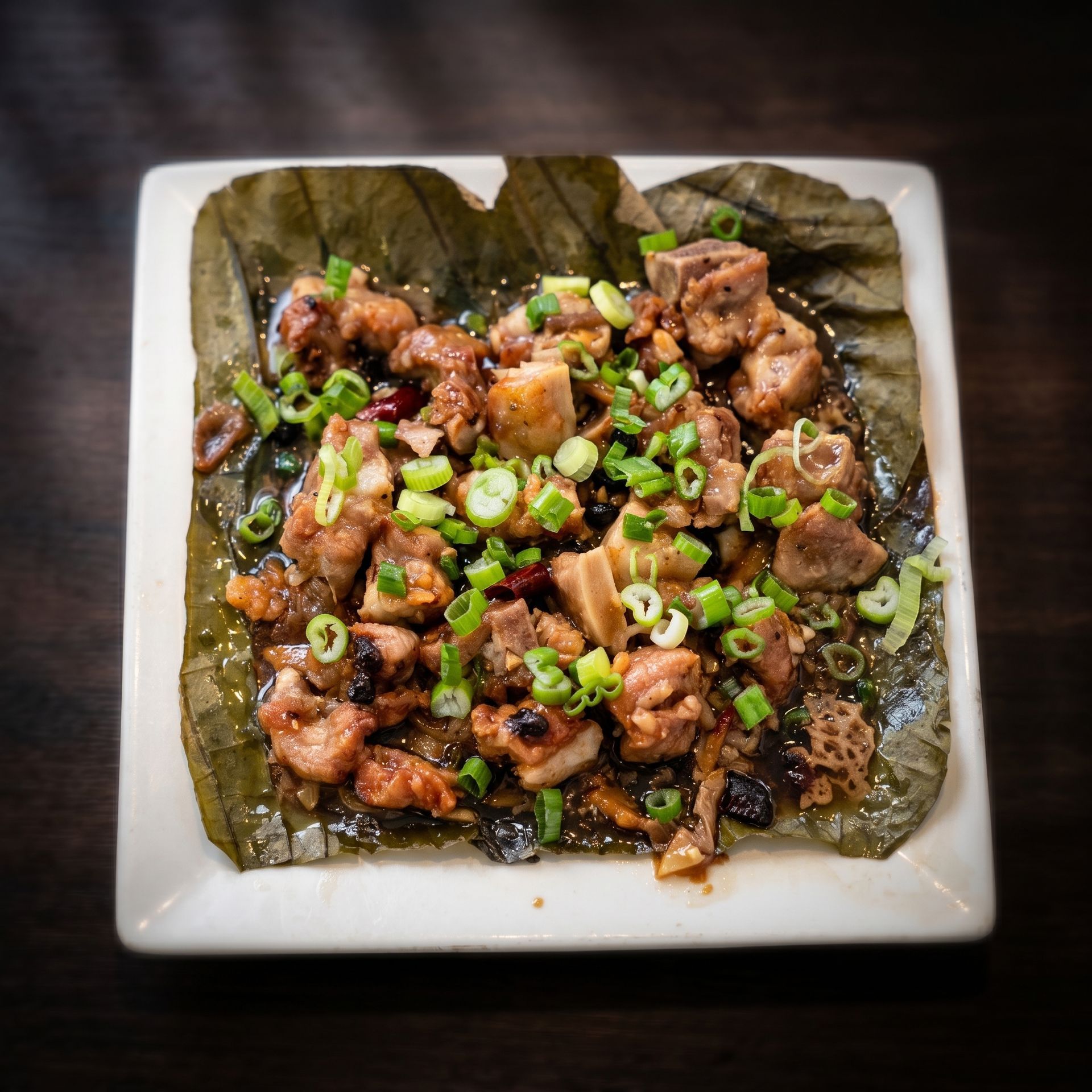 Steamed fish in banana leaf on a white plate, topped with chopped green onions and sauce
