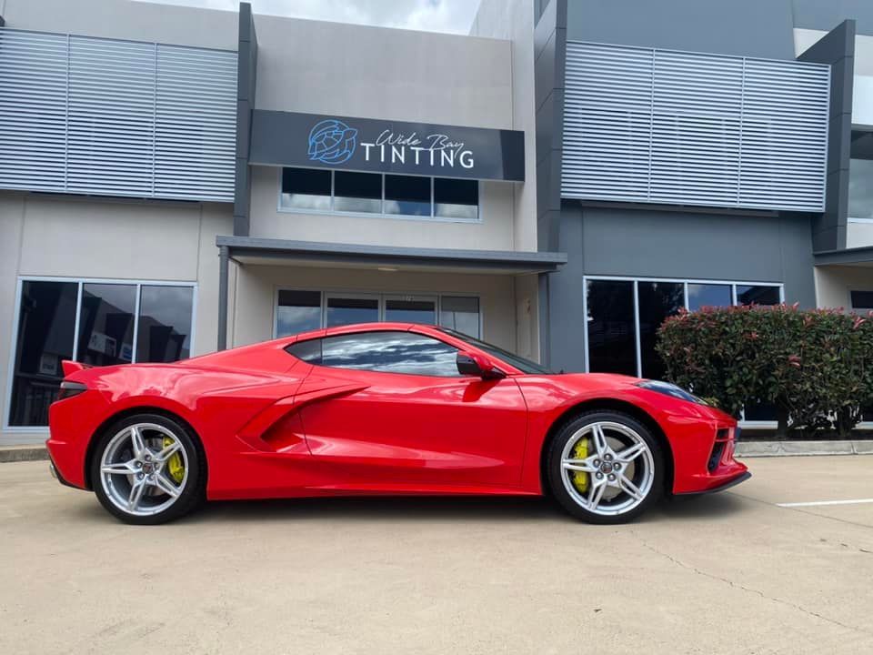 Red sports car with tinted windows parked in front of a building with