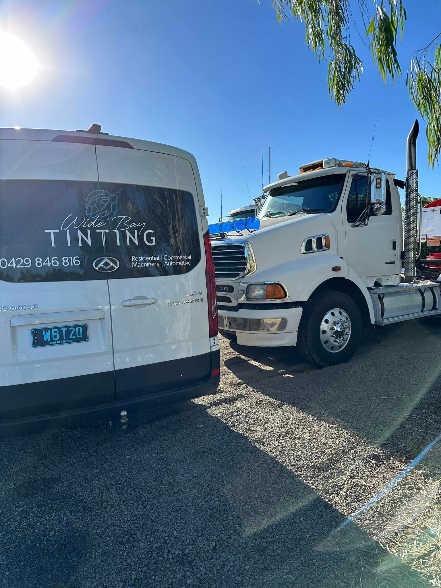White van with tinted window logo next to a white truck on a gravel lot under a bright, sunny sky — Wide Bay Tinting in Kensington, QLD