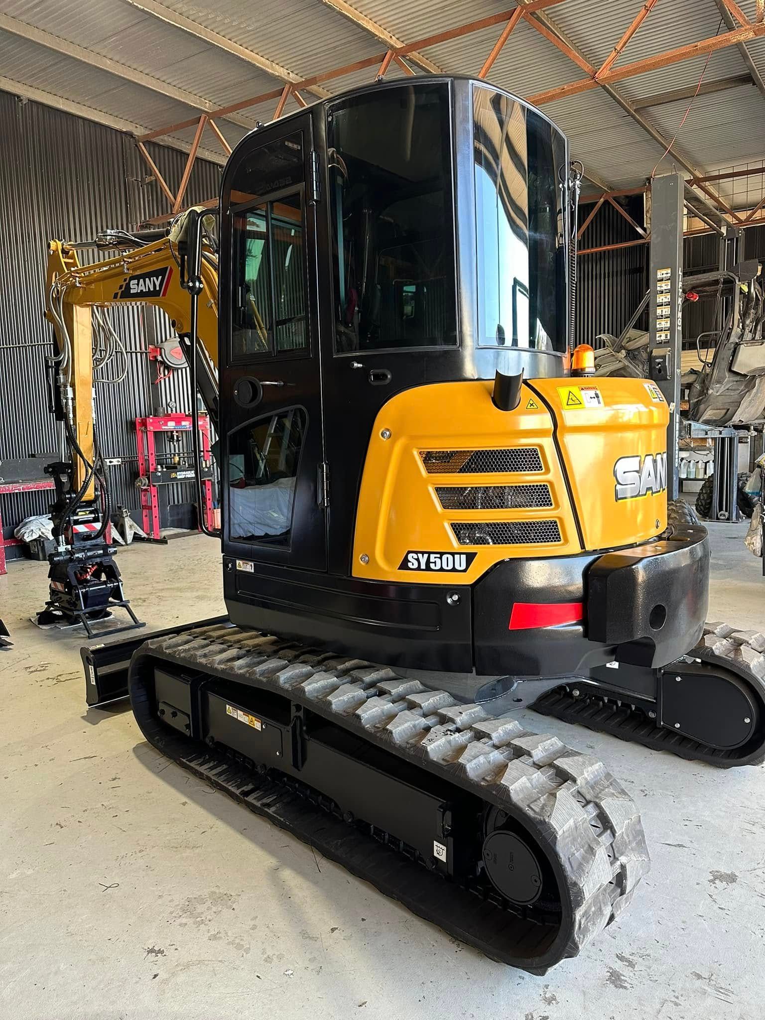 Yellow and Black Excavator on Tracks, Parked Inside a Building — Wide Bay Tinting in Sharon, QLD
