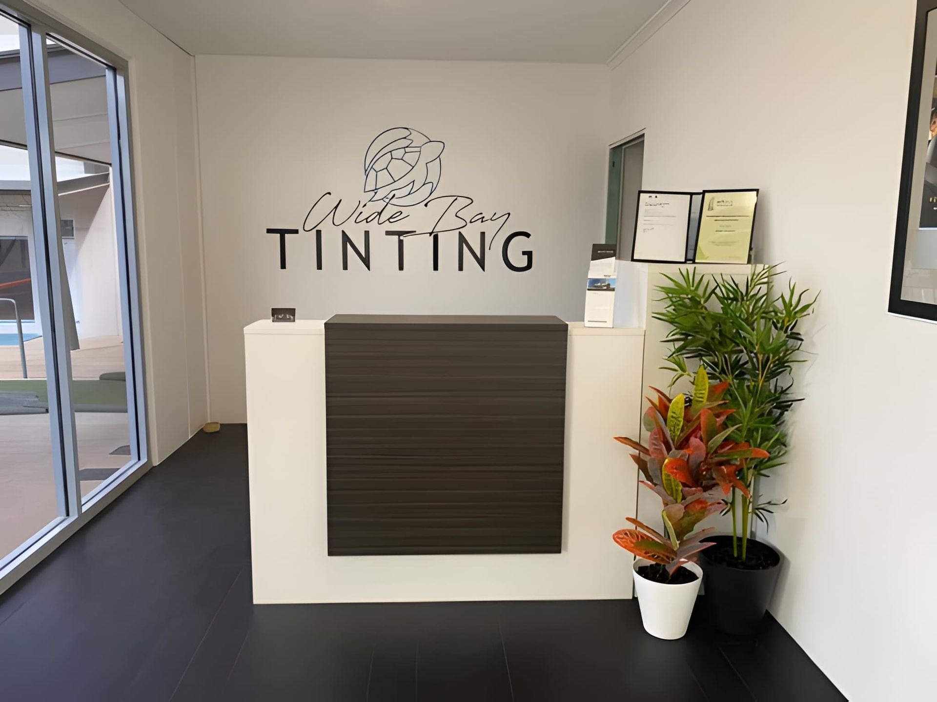 Reception Desk of a Tinting Business, With Logo on the Wall and Plants — Wide Bay Tinting in Kensington, QLD