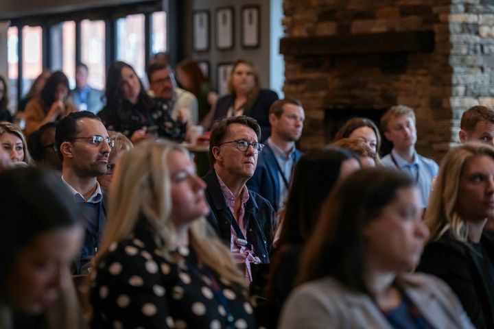 Audience seated at a conference, listening attentively in a warmly lit room
