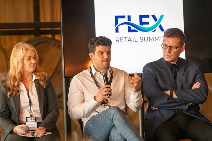 Three speakers on stage at the FLEX Retail Summit, seated and talking into microphones.
