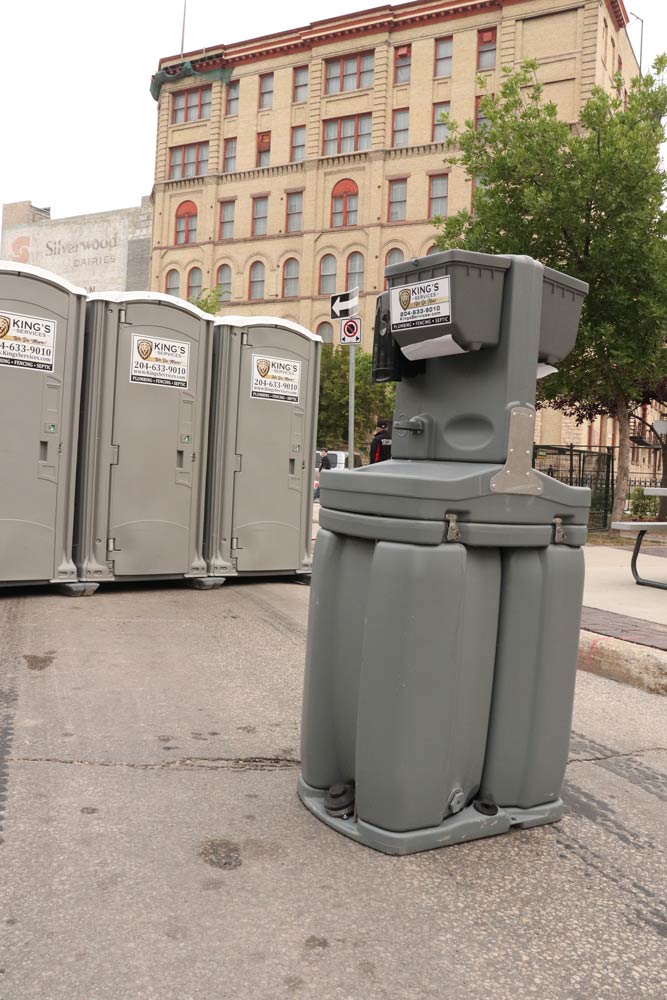 Portable handwashing station and portable toilets in front of a brick building.