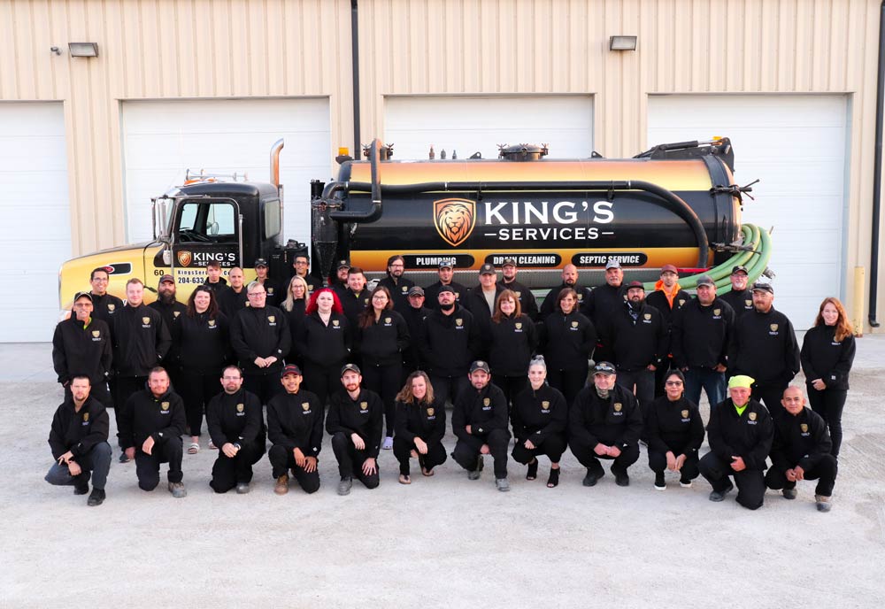 Group of people in black uniforms posing in front of King's Services truck. Building in background.