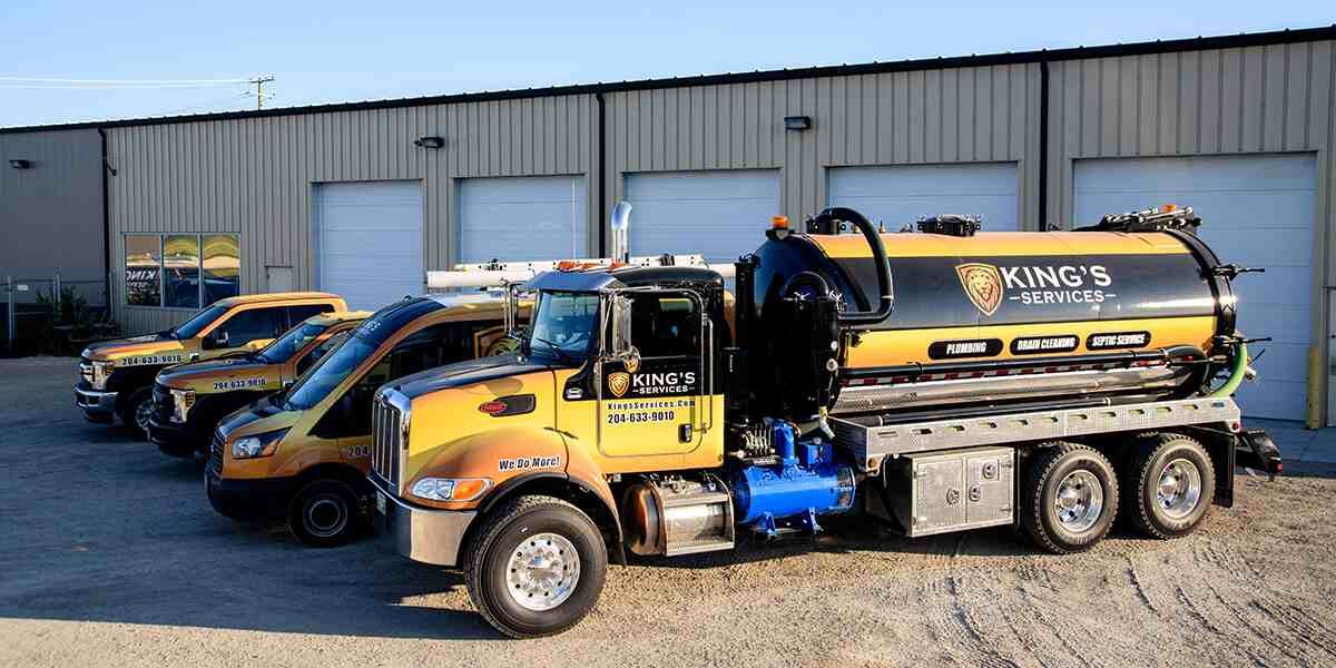 Yellow and black commercial trucks parked in front of a metal building. One is a septic truck labeled “King’s.”