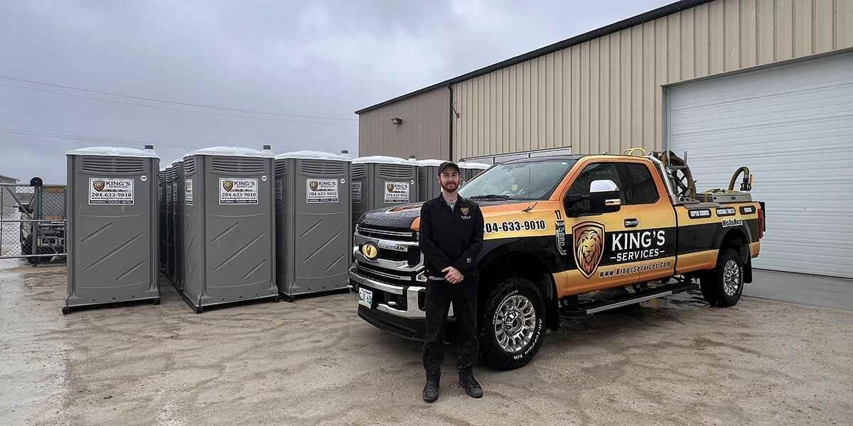 Man standing beside a black-and-orange K9s truck and portable toilets outside a warehouse