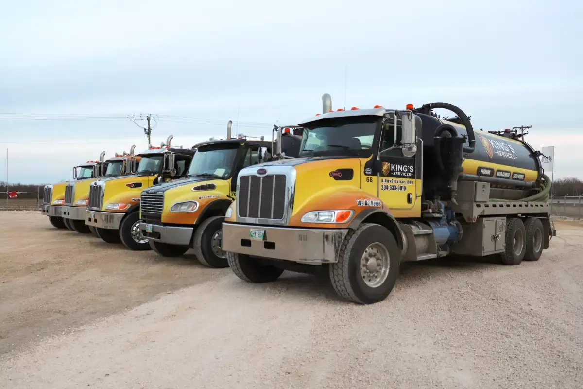 Yellow vacuum trucks lined up on a gravel lot under an overcast sky.