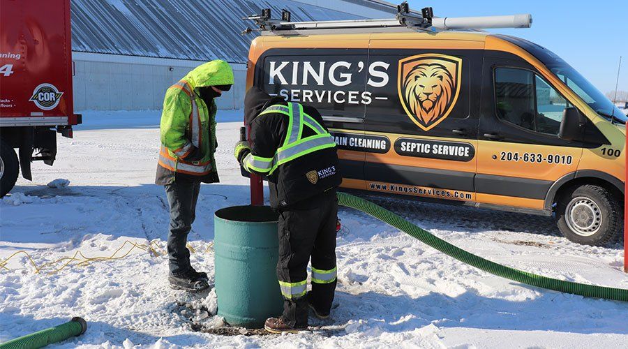 Two people in safety vests working on a septic system in the snow. A van with