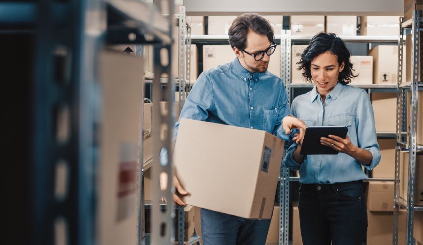 We Box Self Storage Um homem está segurando uma caixa e uma mulher está olhando para um tablet em um armazém.