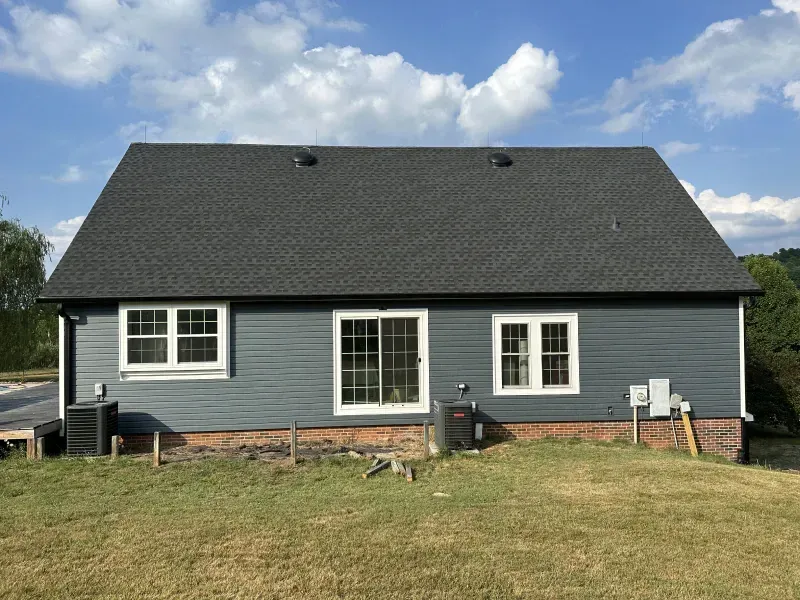 Back view of a gray house with a dark gray roof, two windows, and a sliding glass door against a blue sky.