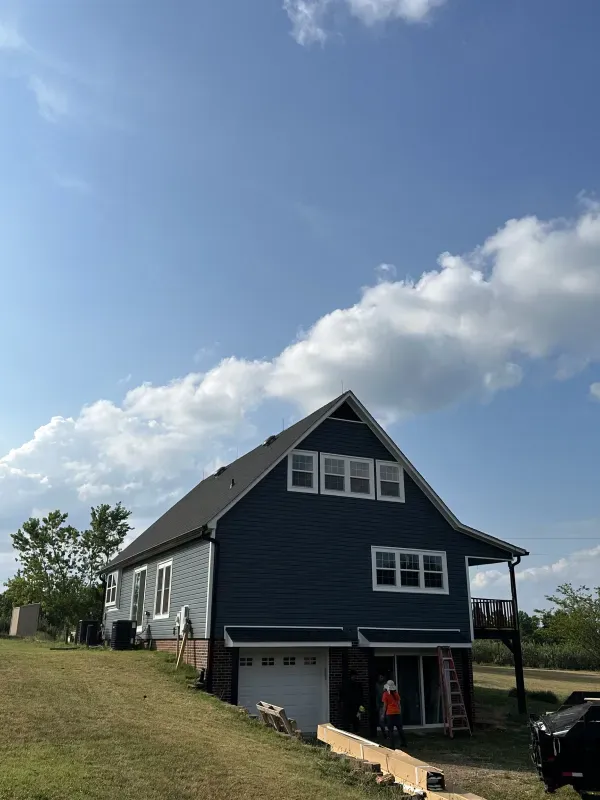 Two-story house with blue and gray siding under a cloudy sky. Garage and small deck visible.