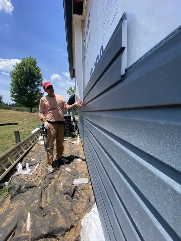 Person installing blue siding on a house exterior; sunny day.