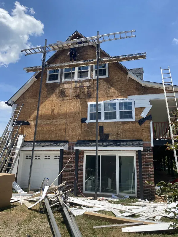 House under construction with scaffolding and a worker; siding being installed on a sunny day.