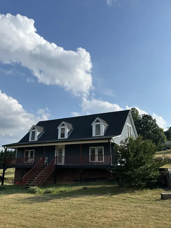 Blue-gray house with white trim, dormers, and a red staircase, set against a blue sky with clouds.
