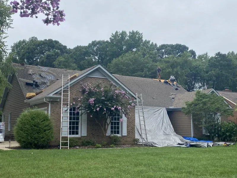 Roofers on a house with a partially removed roof. Ladders, tarp, and shingles are present.