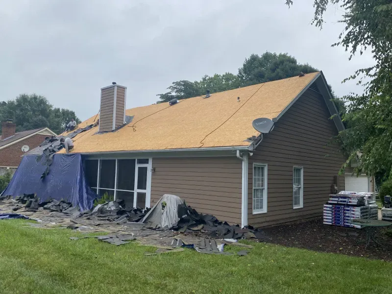 House with partially removed roof, construction debris, and materials on the ground.