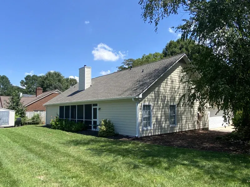 Back view of a light-colored house with a screened porch and chimney, on a sunny day. Green lawn.