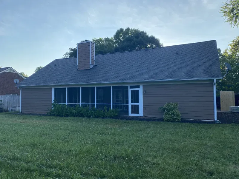 Back of a house with brown siding, screen porch, and a chimney on a sunny day.
