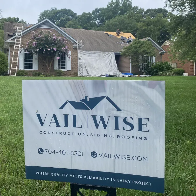 A house with a Vail Wise sign, ladder on the roof, partially covered for repair.