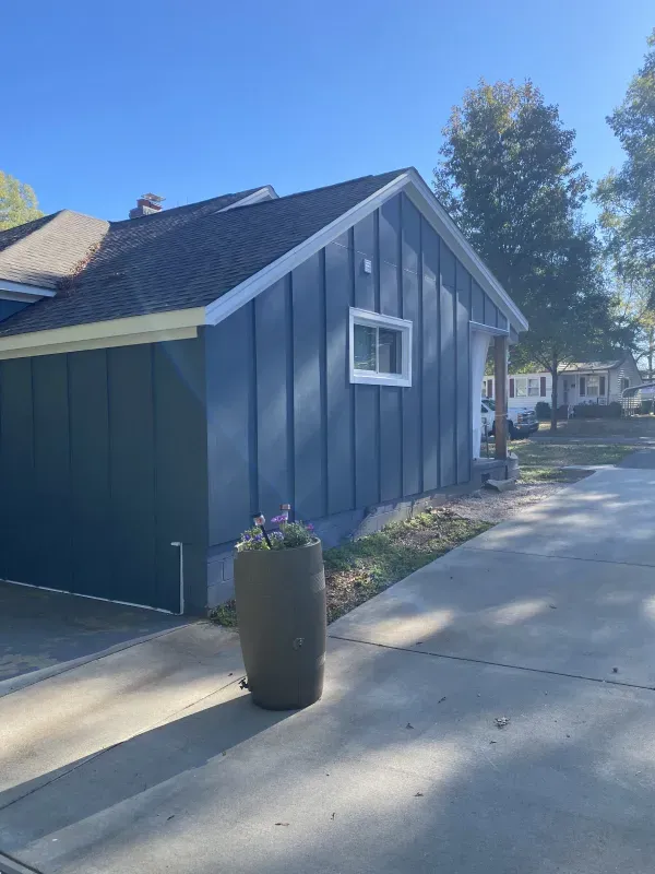 Blue house exterior with vertical siding, white trim, and a concrete driveway.