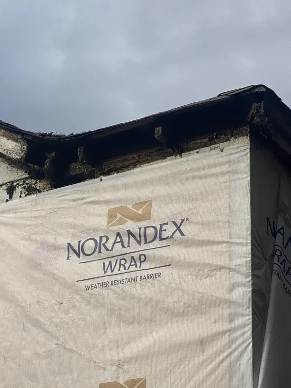 Exterior corner of a building, showing Norandex Wrap weather-resistant barrier and damaged roof edge.