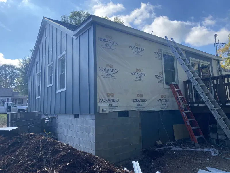 House exterior with dark blue siding being installed, beige section with windows, ladder present.