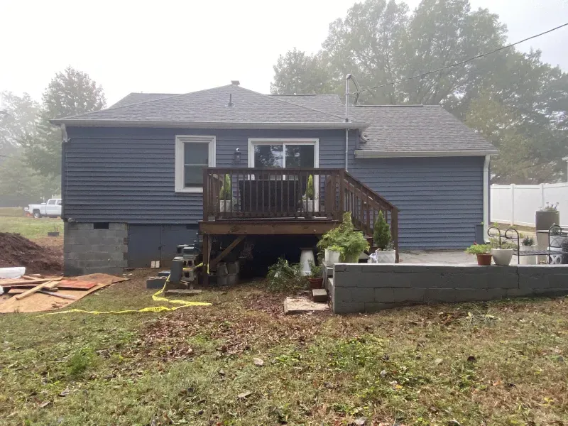 Back of a blue-sided house with a wooden deck; overcast day.