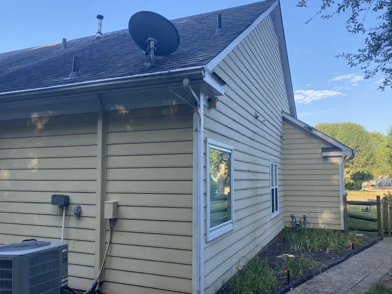 Beige siding house with satellite dish on the roof, windows, gutters, and a grassy area in the background.