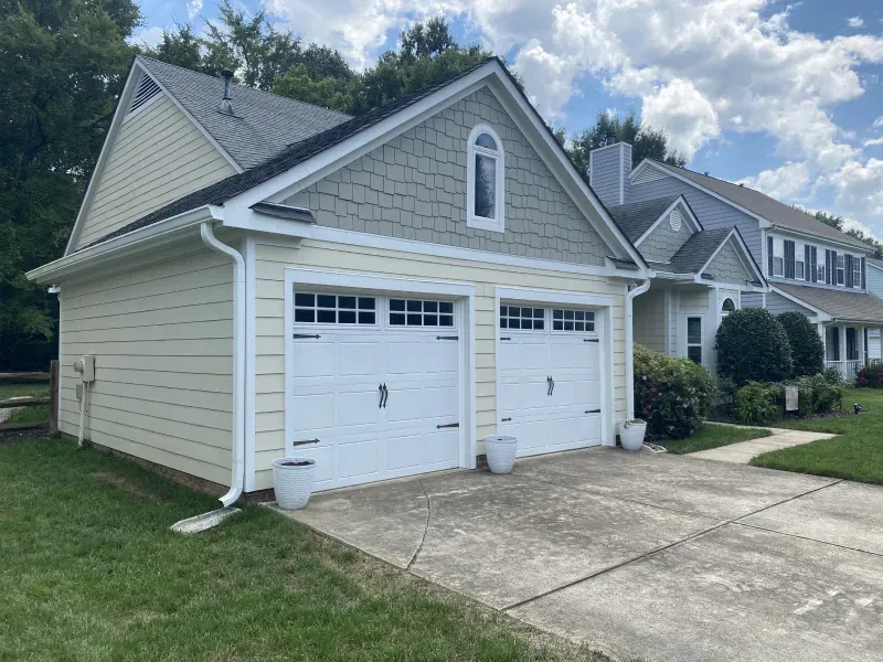 Two-car garage with beige siding, white doors, and a gray roof.
