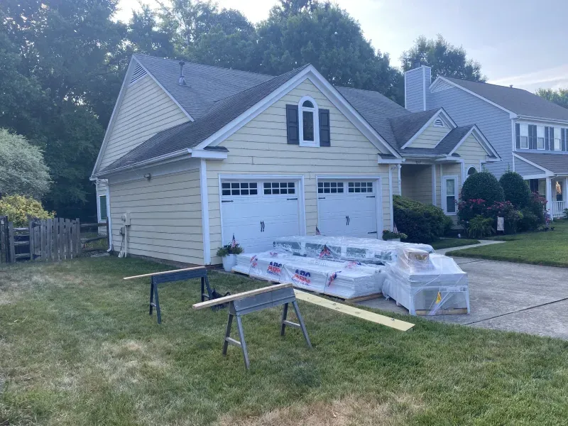 Yellow house with garage doors; lumber, sawhorses in yard; clear sky.